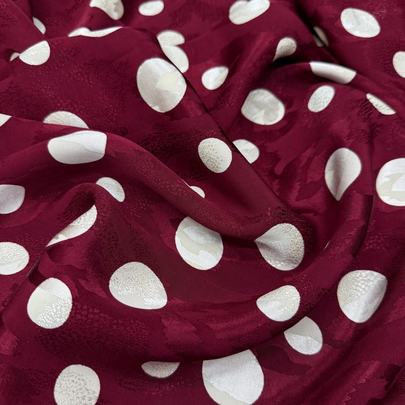 a close-up view of a fabric with a maroon color and white polka dots. The polka dots are scattered across the fabric, creating a playful and festive pattern.