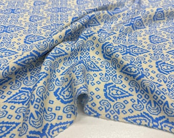 May include: Close-up of a fabric with a repeating blue and white paisley pattern. The fabric is folded, showing the texture and design. The pattern includes teardrop shapes and geometric elements.