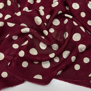 a close-up view of a fabric with a maroon color and white polka dots. The fabric appears to be crumpled and wrinkled, giving it a casual and relaxed appearance.