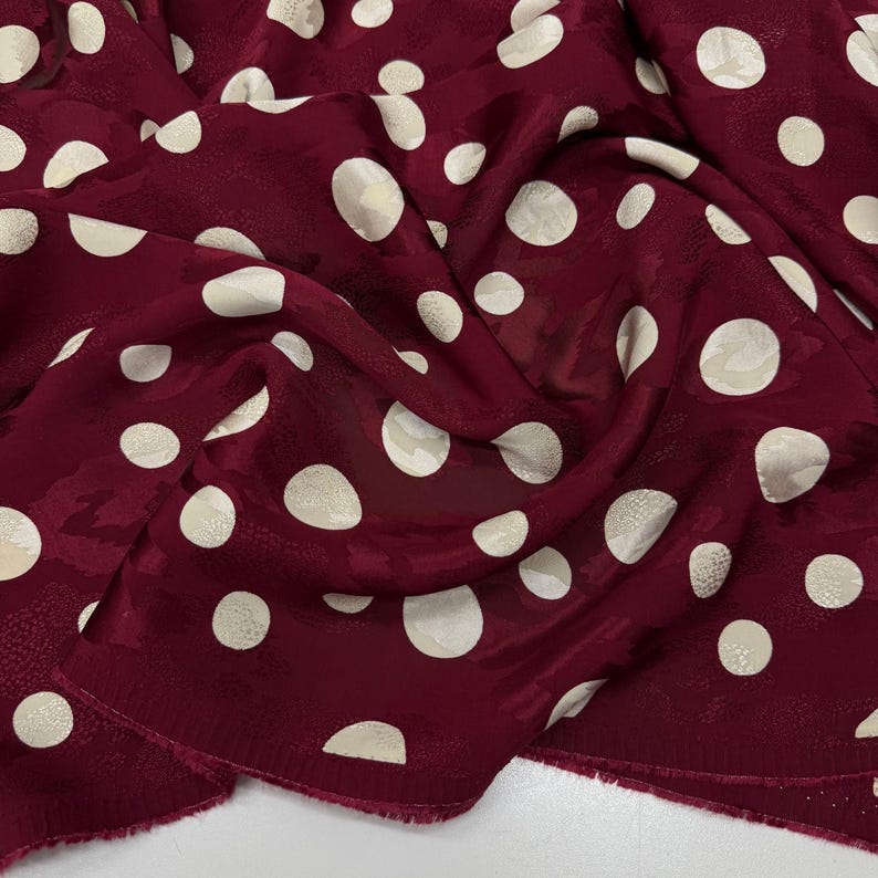 a close-up view of a fabric with a maroon color and white polka dots. The fabric appears to be crumpled and wrinkled, giving it a casual and relaxed appearance.