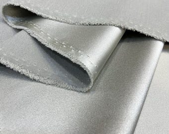 May include: Close-up of a silver satin fabric with a subtle sheen. The fabric is folded and the edges are slightly frayed.