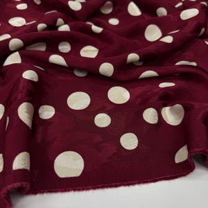 a close-up view of a fabric with a maroon color and white polka dots. The polka dots are scattered across the fabric, creating a playful and festive pattern.