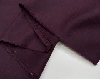 Può includere: Primo piano di un pezzo di tessuto piegato di colore bordeaux scuro. Il tessuto ha una superficie strutturata e un bordo grezzo e non rifinito. Il tessuto è piegato su se stesso, creando più strati.