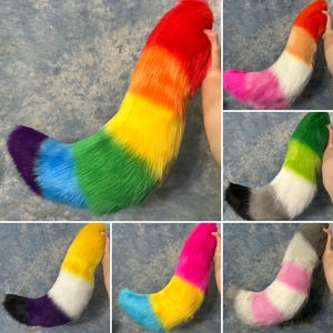May include: A collection of six faux fur tails in various color combinations. The tails feature long, soft synthetic fibers arranged in horizontal stripes of red, orange, yellow, green, blue, purple, pink, white, gray, and black.