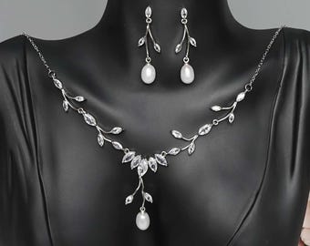 May include: A silver necklace and earrings set with a delicate leaf design and pearl accents.