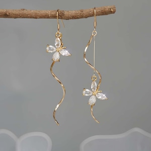 May include: A pair of gold-toned dangle earrings featuring a delicate spiral wire design. One earring displays a butterfly-shaped charm crafted from four marquise-cut clear crystals, while the other features a longer spiral wire with a butterfly charm.