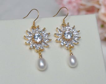 May include: Gold dangle earrings with a pearl drop and a flower-shaped cluster of clear cubic zirconia stones.