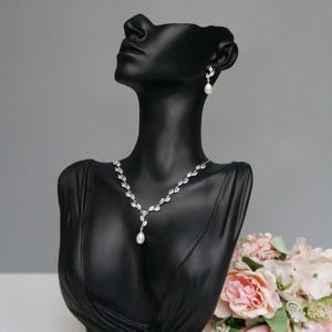以下が含まれることがあります： 真珠のドロップペンダントと葉の形をしたクリスタルアクセントが付いたシルバーネックレスとイヤリングのセットです。