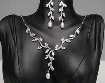 May include: A silver necklace and earrings set with a leaf design and pearl accents. The necklace has a long pendant with a pearl at the end.