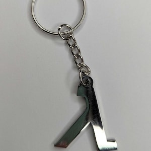 Puede incluir: Un llavero de metal plateado con el símbolo Lambda de la serie de videojuegos Half-Life.