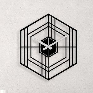 May include: A black geometric wall clock with white hands, hanging on a white wall above a modern coffee table with a vase of pink flowers and candles.