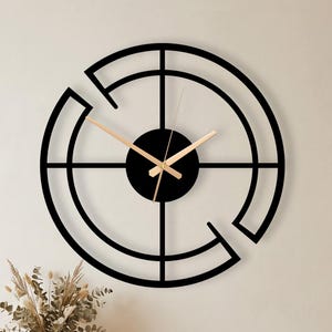 May include: A large circular wall clock featuring a black metal frame with an open geometric design consisting of concentric arcs and intersecting lines. The clock has a solid black center hub and thin, light-colored metallic hands.
