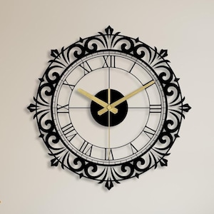 May include: A large black and gold wall clock with Roman numeral markings and an intricate decorative frame. The clock is hanging on a white wall above a wooden cabinet.