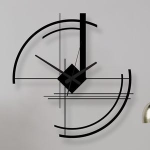May include: A modern black wall clock with a geometric design hangs on a gray wall. The clock features a square center and curved lines. Two white wire chairs and a small table with a chess set are in front of the wall.
