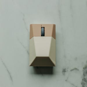 Puede incluir: Un peque&ntilde;o rat&oacute;n de ordenador beige y marr&oacute;n claro con un dise&ntilde;o geom&eacute;trico. El rat&oacute;n tiene una sola rueda de desplazamiento.