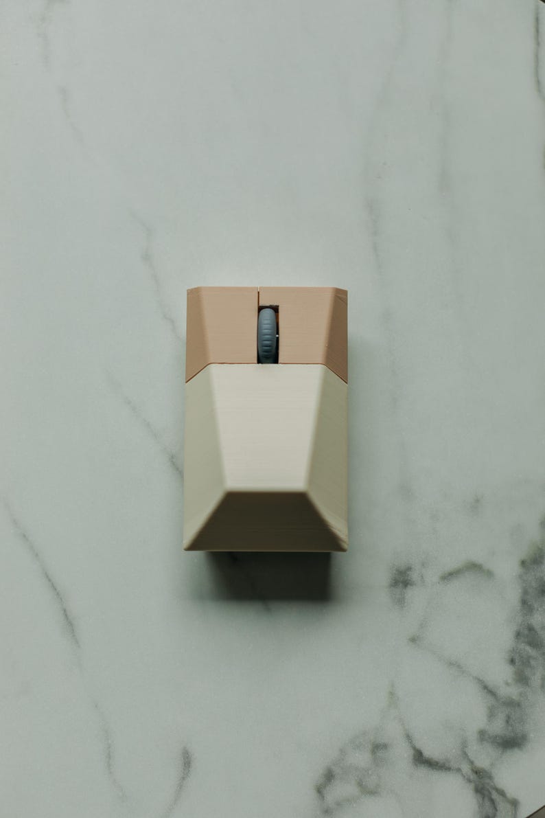 Puede incluir: Un peque&ntilde;o rat&oacute;n de ordenador beige y marr&oacute;n claro con un dise&ntilde;o geom&eacute;trico. El rat&oacute;n tiene una sola rueda de desplazamiento.