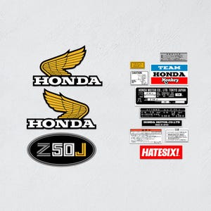 Pode incluir: Uma coleção de adesivos para motocicleta Honda incluindo dois logotipos de asas amarelas, um emblema oval Z50J e várias etiquetas retangulares de informações técnicas com texto como Team Honda Monkey, Honda Motor Co. Ltd. Tokyo Japan e Hatesix.