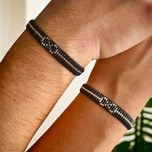 May include: Two black and white beaded bracelets on a person's wrists. The bracelets have a geometric pattern.