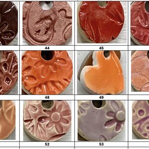May include: A collection of ceramic pendants with various textures and colors. The pendants are round with a hole at the top for hanging. Colors include red, orange, brown, and purple. Some pendants have floral or leaf patterns.