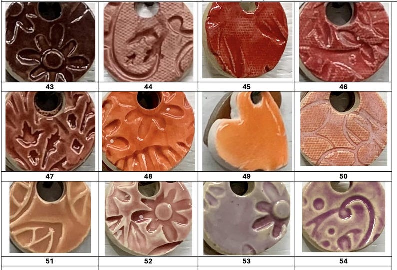 May include: A collection of ceramic pendants with various textures and colors. The pendants are round with a hole at the top for hanging. Colors include red, orange, brown, and purple. Some pendants have floral or leaf patterns.