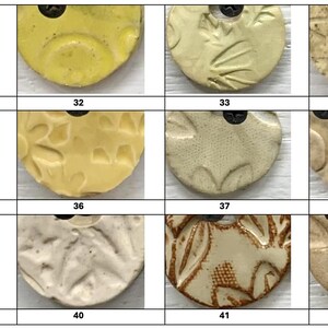 May include: A collection of ceramic pendants with various textures and colors. The pendants are round with a hole at the top for hanging. Colors include yellow, beige, and off-white. The textures include leaf patterns, dots, and abstract designs.