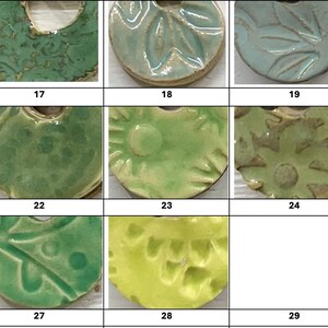 May include: A collection of ceramic pendants in various shades of green, blue, and yellow. Each pendant has a unique design, including floral patterns, swirls, and textured surfaces. The pendants are numbered 16 through 30.