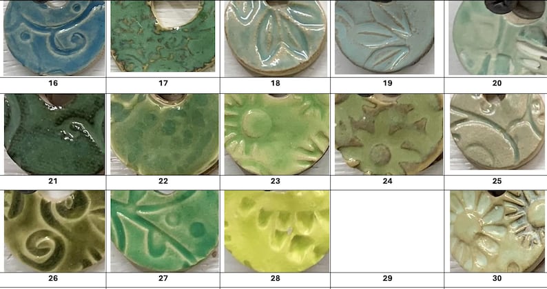 May include: A collection of ceramic pendants in various shades of green, blue, and yellow. Each pendant has a unique design, including floral patterns, swirls, and textured surfaces. The pendants are numbered 16 through 30.