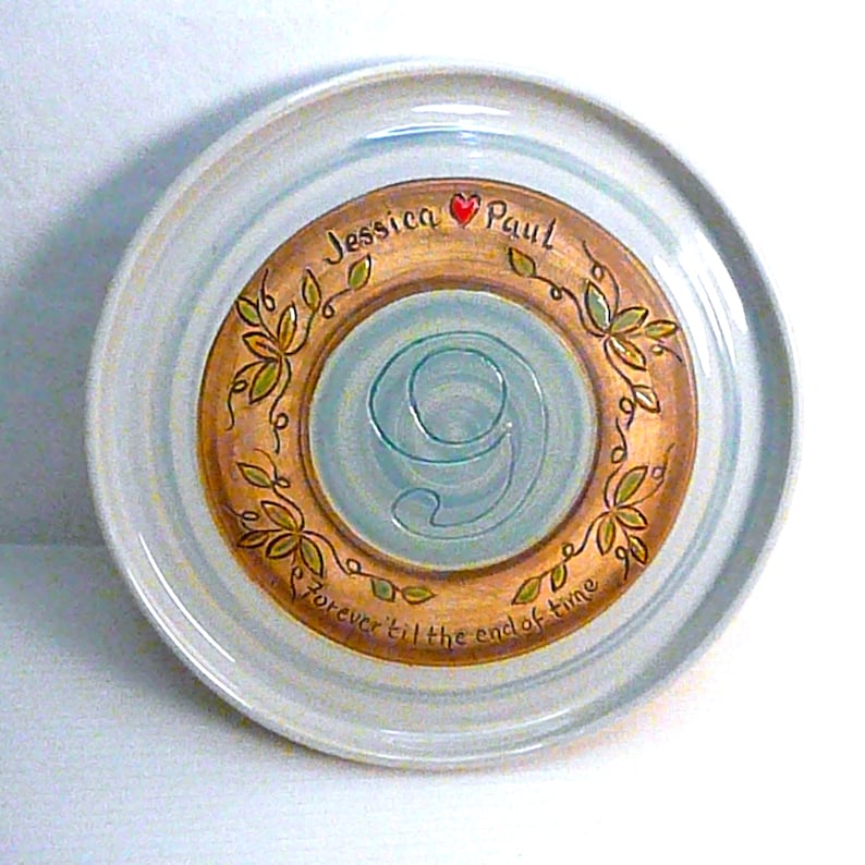 May include: A decorative ceramic plate with a light blue rim and a central design. The center features a light blue number 9, surrounded by a gold-colored ring with the names "Jessica Paul" and the phrase "forever til the end of time".