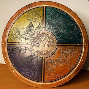 May include: A circular wooden shield featuring a central embossed tree of life surrounded by four quadrants. Each quadrant displays a different animal: a deer in yellow, a wolf in green, a raven in purple, and a horse in brown, all with intricate knotwork.