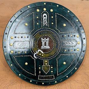 May include: A round, dark green shield with a central design featuring a white castle and the words "VIRTUE HONOR". The shield is adorned with gold-colored studs and decorative patterns, creating a medieval aesthetic.