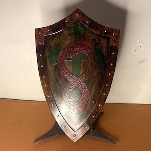 May include: A wooden shield with a red and green dragon design. The shield is mounted on a black metal stand.