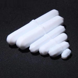 May include: A selection of white magnetic stirrers, cylindrical in shape and of different sizes, set against a dark backdrop. These laboratory tools are used for mixing liquids and have a smooth, glossy appearance.