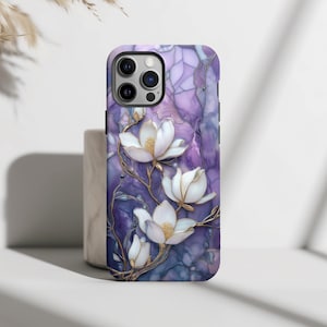 May include: A phone case with a floral design. The case features a purple and blue marble background with white magnolia flowers and gold accents. The case has a glossy finish and is designed for a smartphone.