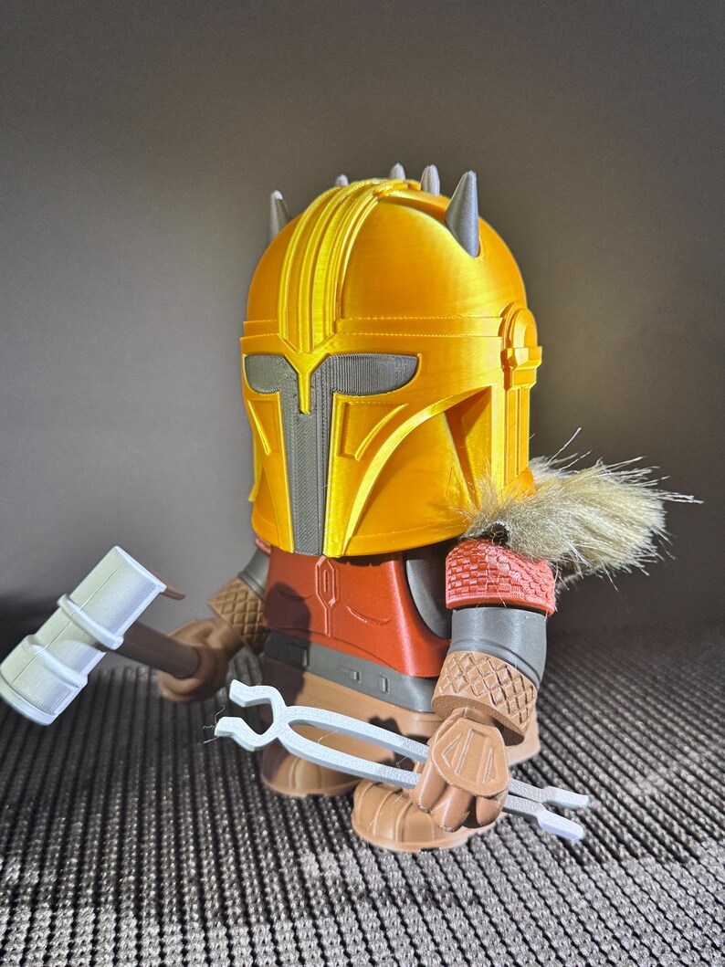 May include: A 3D-printed figure of a character in a yellow helmet with grey accents, wearing a red and brown outfit. The figure holds a white hammer and tongs. The figure has a fur collar.