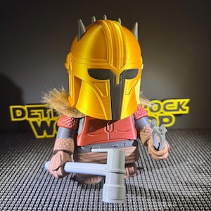 May include: A figurine of a character in a gold helmet, red armour, and a brown fur collar. The figure holds a grey hammer and a small tool. The background is black with yellow text.
