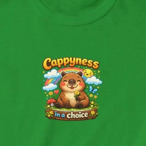 K&ouml;nnte beinhalten: Gr&uuml;nes Sweatshirt mit einem Cartoon-B&auml;ren, der eine Blume h&auml;lt, mit dem Text "Cappyness in a choice". Das Design umfasst einen Regenbogen, eine Sonne, Wolken und Blumen, was eine fr&ouml;hliche und skurrile &Auml;sthetik schafft.