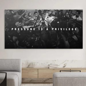 May include: Black and white photograph of a person surrounded by microphones and cameras. The text "PRESSURE IS A PRIVILEGE" is displayed in white block letters across the top of the image. The image is mounted on a wall.