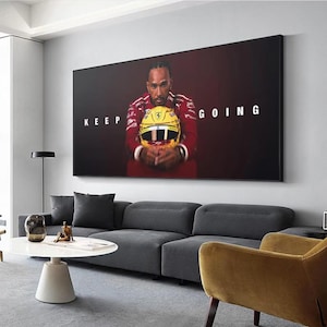Puede incluir: Un gran cuadro enmarcado con un piloto de Fórmula 1 sosteniendo un casco amarillo. El cuadro tiene las palabras "KEEP GOING" en texto blanco. El piloto lleva un traje de carreras rojo. El fondo es rojo oscuro.