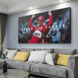 Può includere: Stampa artistica da parete incorniciata con un pilota di Formula 1 in tuta rossa, con le braccia alzate in segno di vittoria. La stampa include le parole "NEVER SETTLE" in testo bianco. L'immagine è sopra un divano grigio.