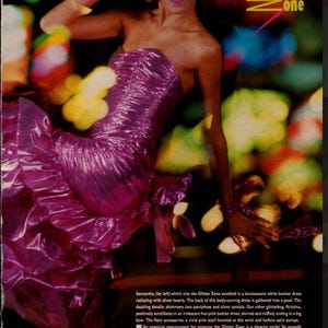 May include: A woman in a shiny, hot-pink bustier dress with a ruffled skirt and a big bow. The dress is part of a fashion spread titled "The Glitter Zone". The image has a vintage aesthetic with blurred background lights.
