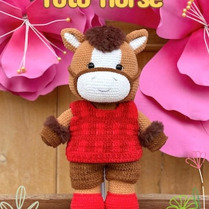 May include: A handmade crochet horse doll with the text "Toto Horse". The horse has a brown and white head, a red vest, brown shorts, and red shoes. The doll is set against a backdrop of pink flowers.
