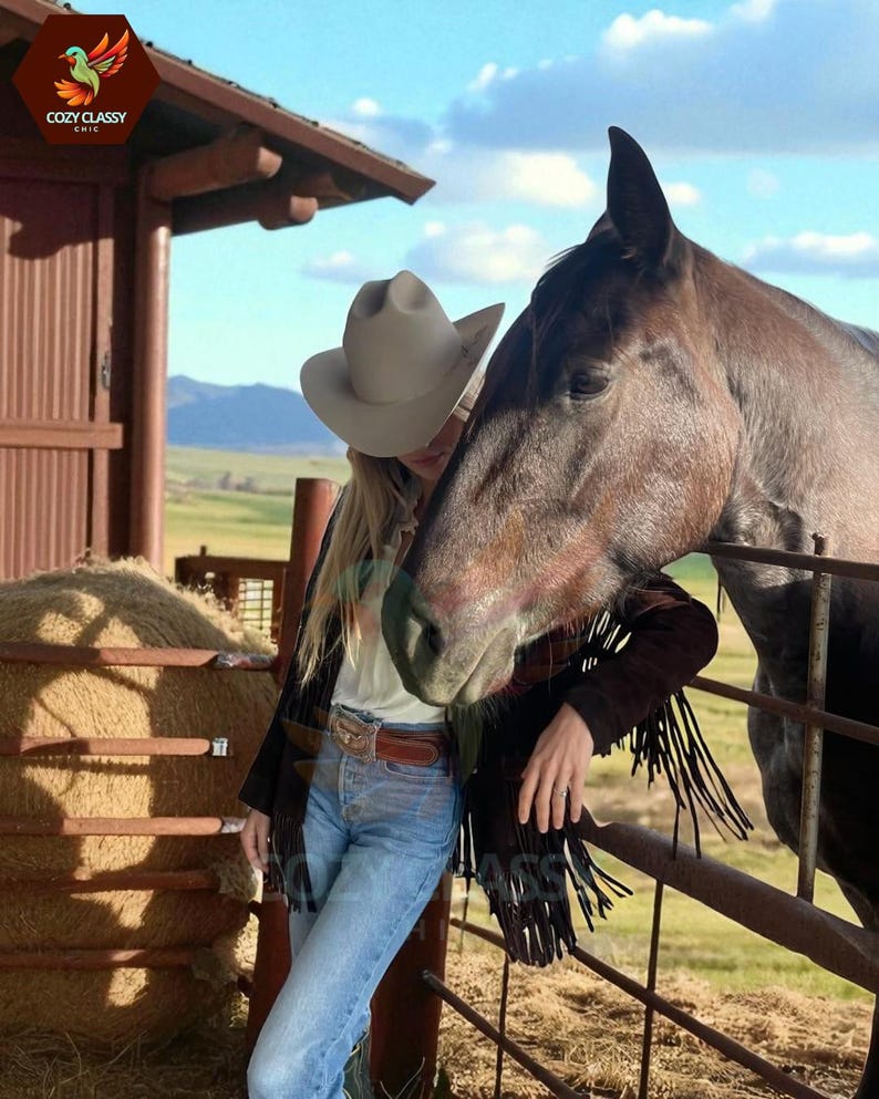 K&ouml;nnte beinhalten: Eine Person mit hellem Cowboyhut, schwarzer Jacke mit Fransen und blauer Jeans, die sich an einen Metallzaun neben einem braunen Pferd lehnt. Die Szene spielt sich im Freien mit einer Scheune und einem Feld im Hintergrund ab.