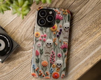 May include: A white iPhone case with a floral pattern and skeletons. The flowers are pink, yellow, orange, and blue. The skeletons are white and have a 3D effect.