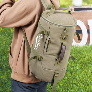 May include: A green canvas duffel bag with a brown leather handle and adjustable straps. The bag has a white embroidered logo that says "Cartier".