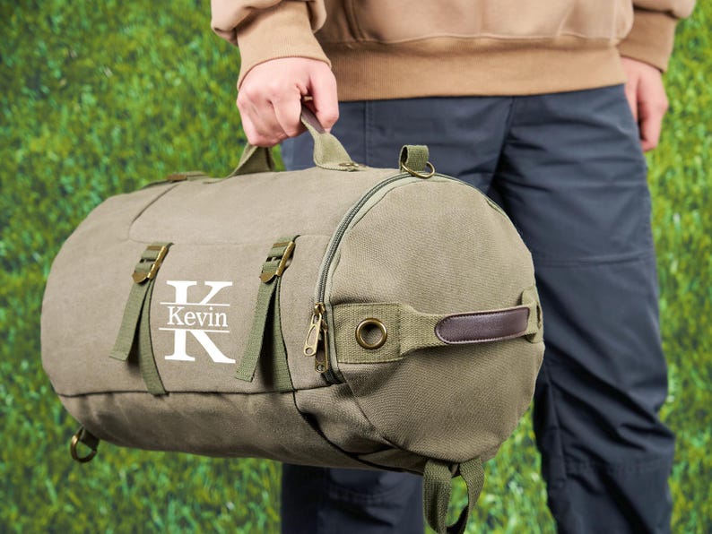 May include: A green canvas duffel bag with a brown leather handle and a zipper closure. The bag has a white monogram with the letter "K" and the name "Kevin" printed on it.