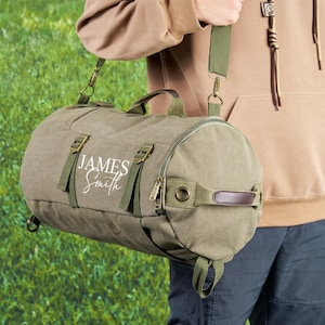 May include: A green canvas duffel bag with a brown leather handle and adjustable shoulder strap. The bag has a white embroidered name "JAMES Smith" on the front.