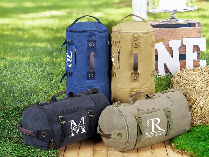 May include: Four personalized canvas duffel bags in blue, tan, black, and green. The bags have a large initial and name embroidered on the front. The bags have a top handle and adjustable shoulder straps.