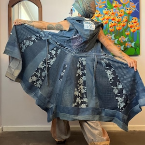 Könnte beinhalten: Ein Patchwork-Jeanskleid mit verschiedenen Blautönen und floralen Mustern. Das Kleid hat ein ärmelloses Oberteil und einen ausgestellten Rock, mit einem Gürtel in der Taille. Das Kleid besteht aus recyceltem Denim.