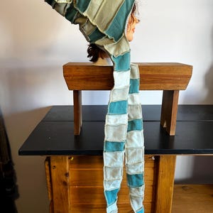 Peut inclure: Ensemble capuche et écharpe patchwork dans les tons de vert d'eau, crème et vert olive. La capuche est pointue et l'écharpe est longue et rectangulaire, avec un motif patchwork. L'ensemble est présenté sur une tête de mannequin.