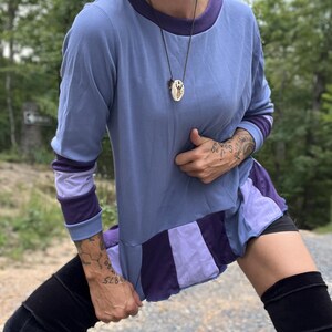 Peut inclure: Un haut bleu à manches longues avec une bordure violette et un motif color-block à l'ourlet. Le haut est associé à des cuissardes noires. Un collier pendentif est suspendu au cou.